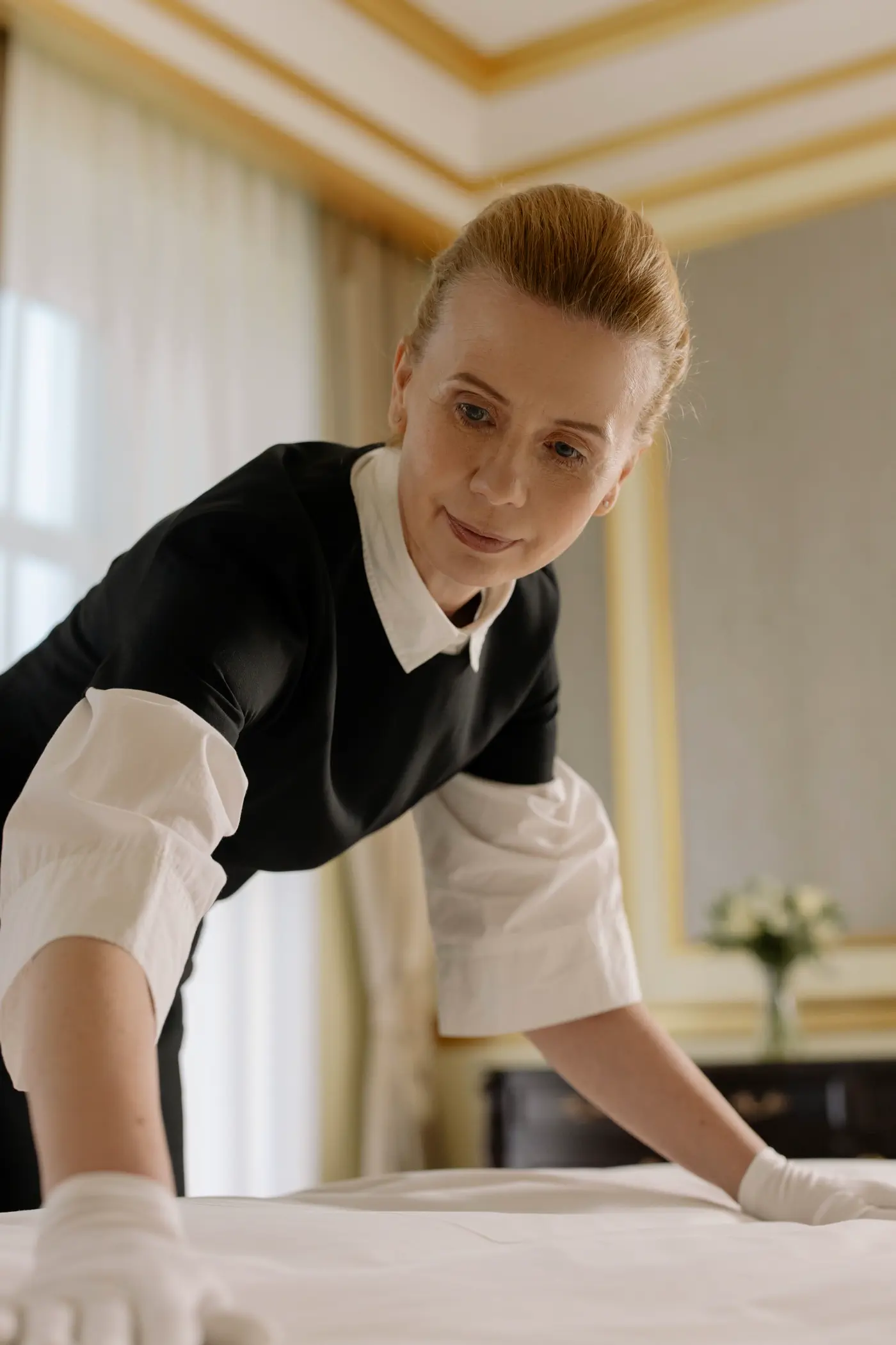 cottonbro studio / Pexels Hotel attendant in uniform arranging bed linen — licensed Pexels still, not a job site